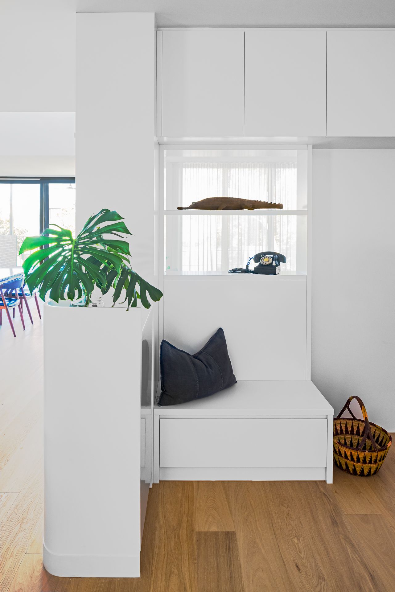 Bright white entryway with built-in bench seat, navy cushion, vintage rotary phone, monstera plant and woven basket on timber floor.