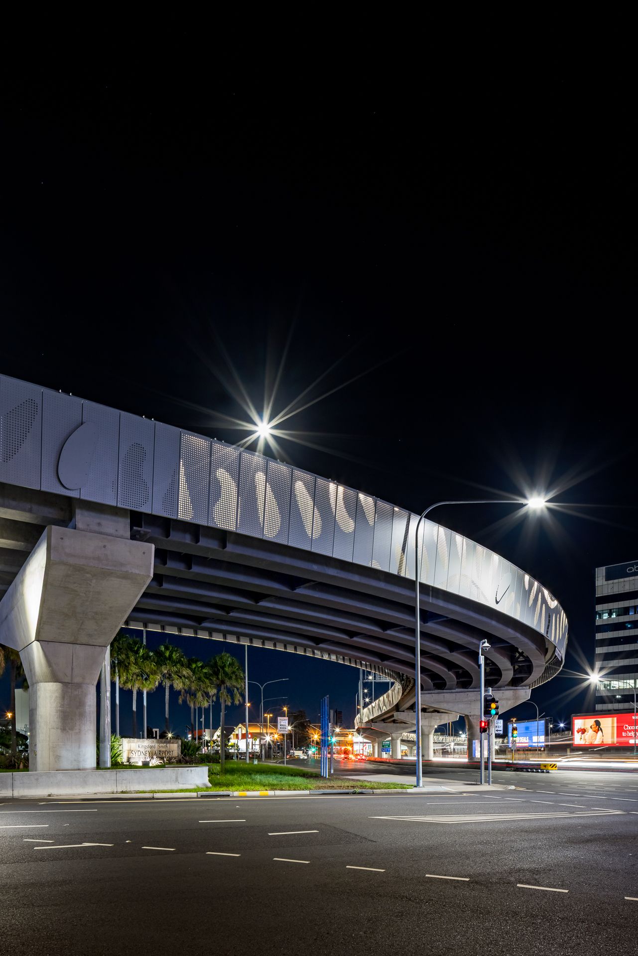 Curved elevated roadway with a patterned concrete facade and concrete piers, lit by streetlights at night.