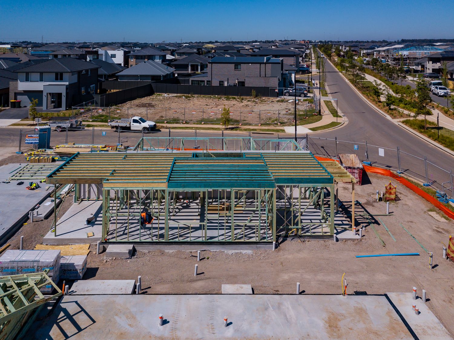 Aerial view of a new home framing under construction on a suburban estate lot with a road and finished houses nearby.