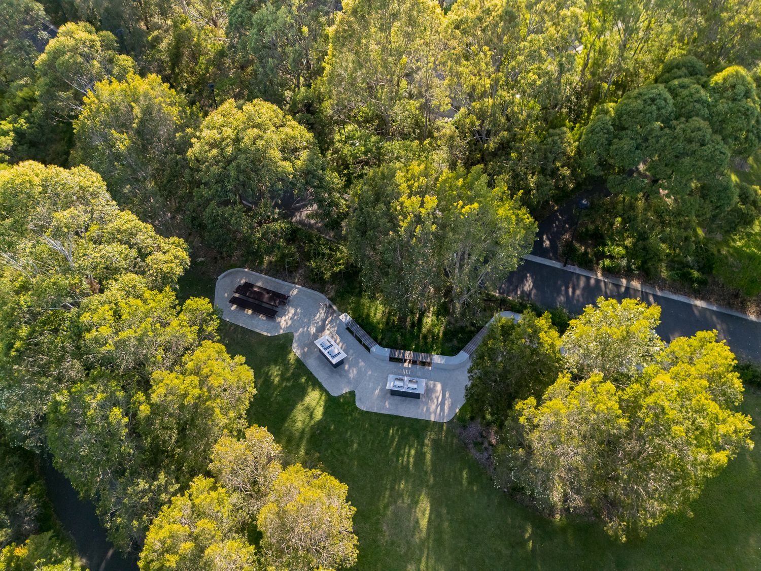 Aerial view of a small paved lookout with seating tucked among lush green trees and a curving road in Sydney Park.
