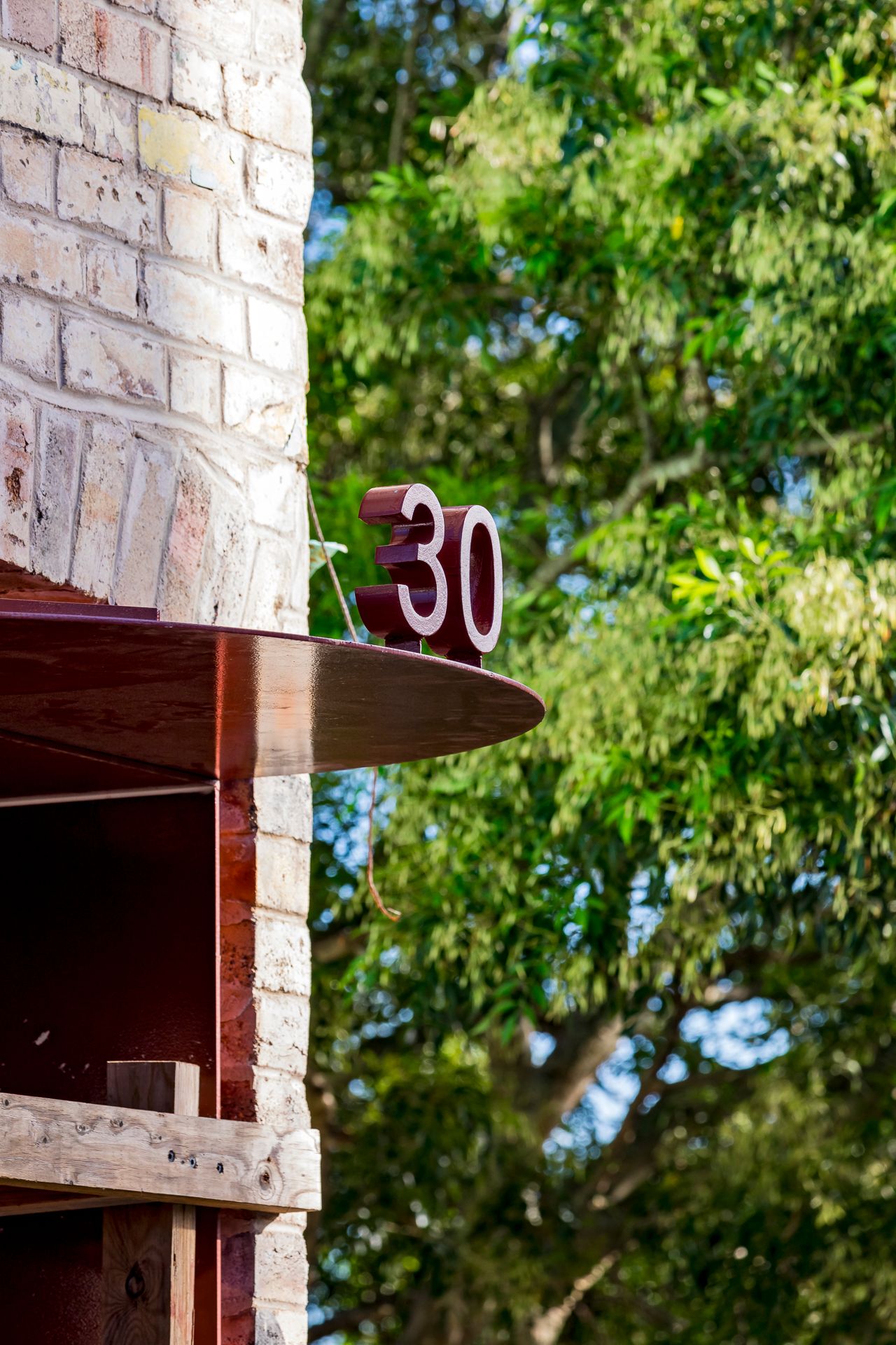 Red number 30 on a brick wall corner beside a curved red canopy with green tree foliage behind.