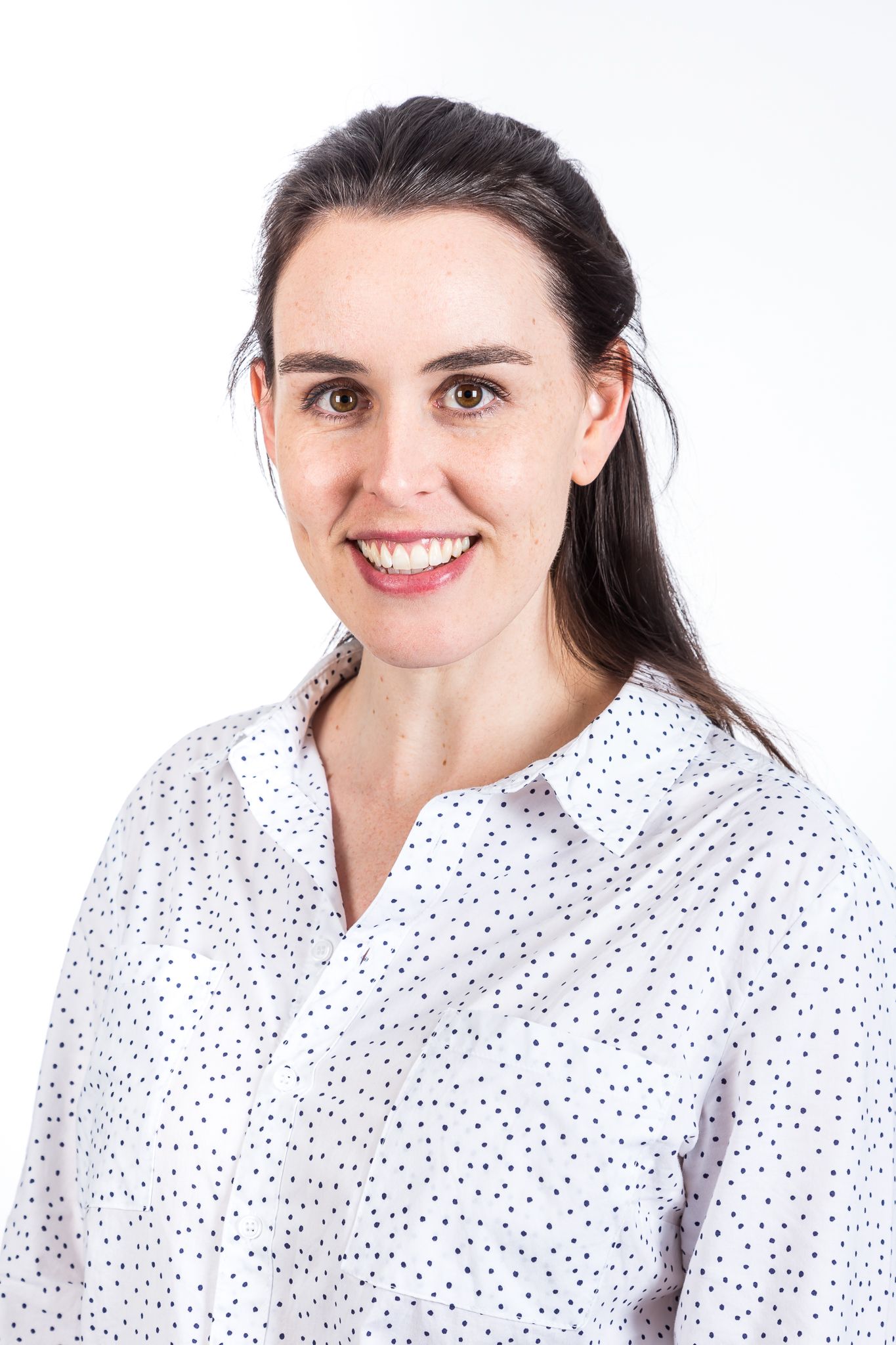 Smiling woman with dark hair pulled back wearing a white polka dot blouse in a professional headshot against a white background.