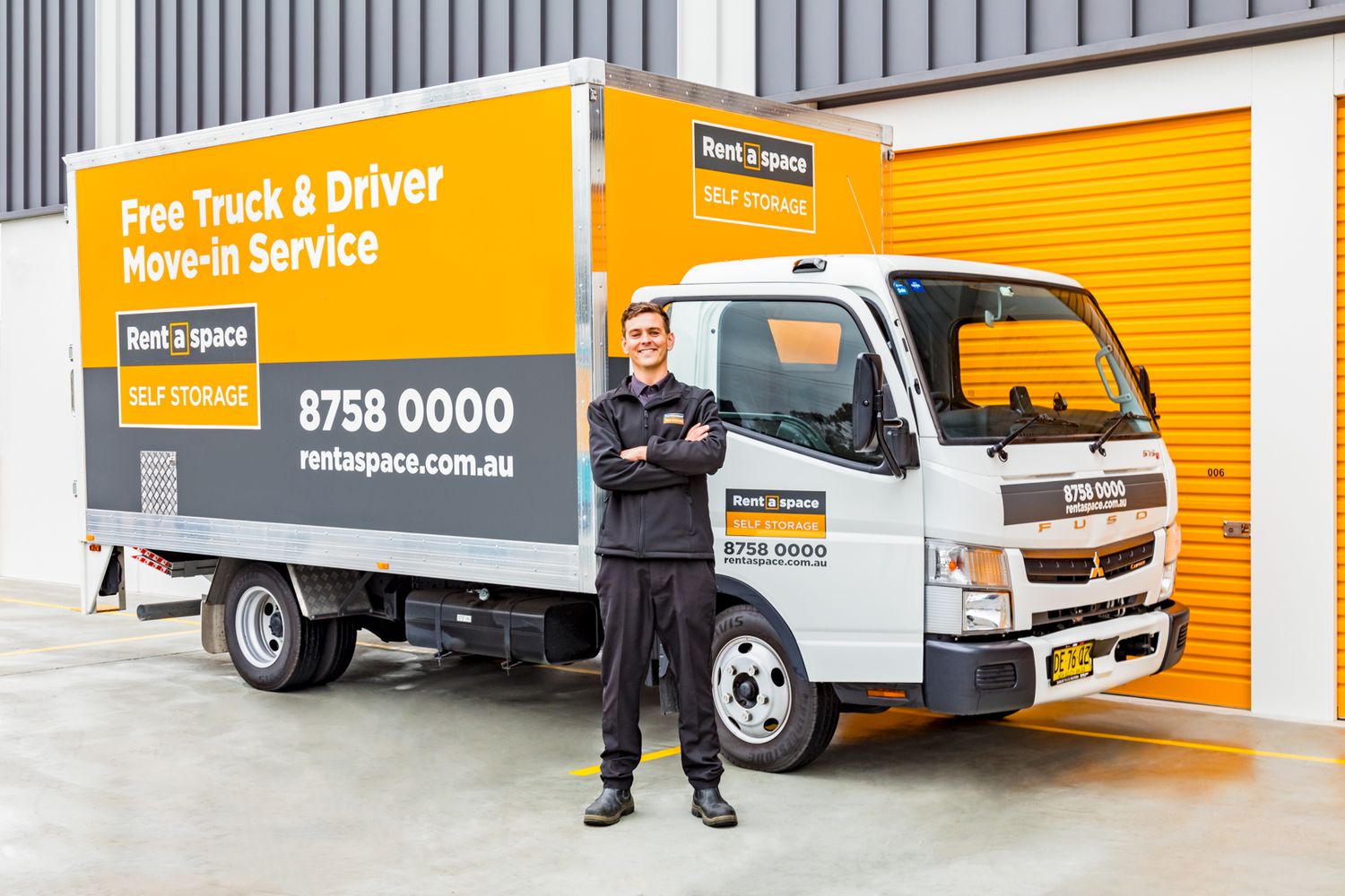 Smiling man with crossed arms beside an orange Rent a space self storage truck offering a free truck and driver move-in service.