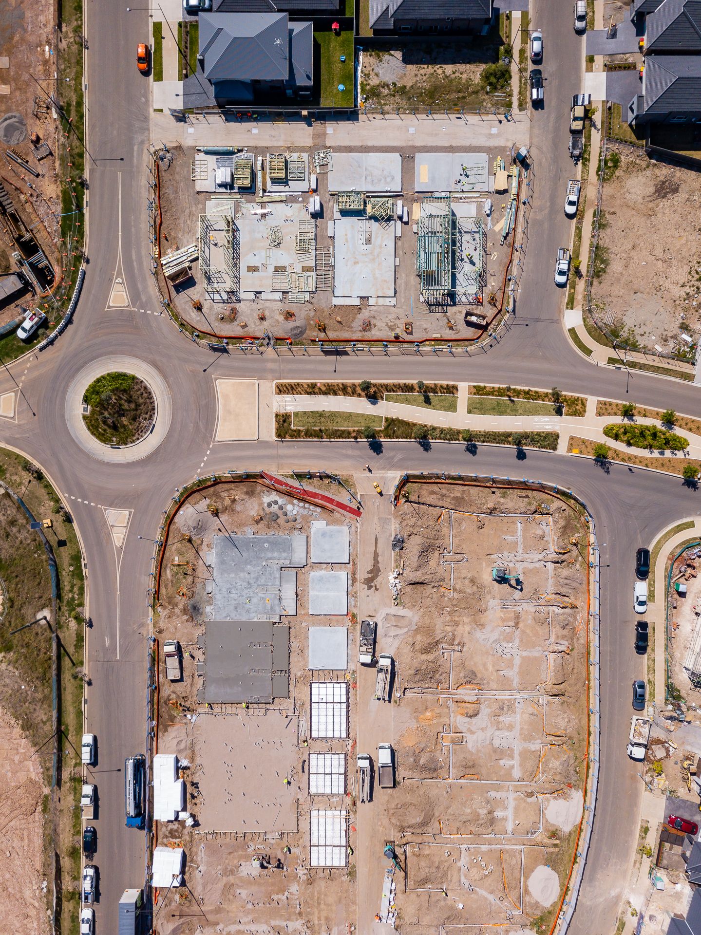 Aerial view of a residential construction site with a roundabout, new house foundations and surrounding suburban streets.