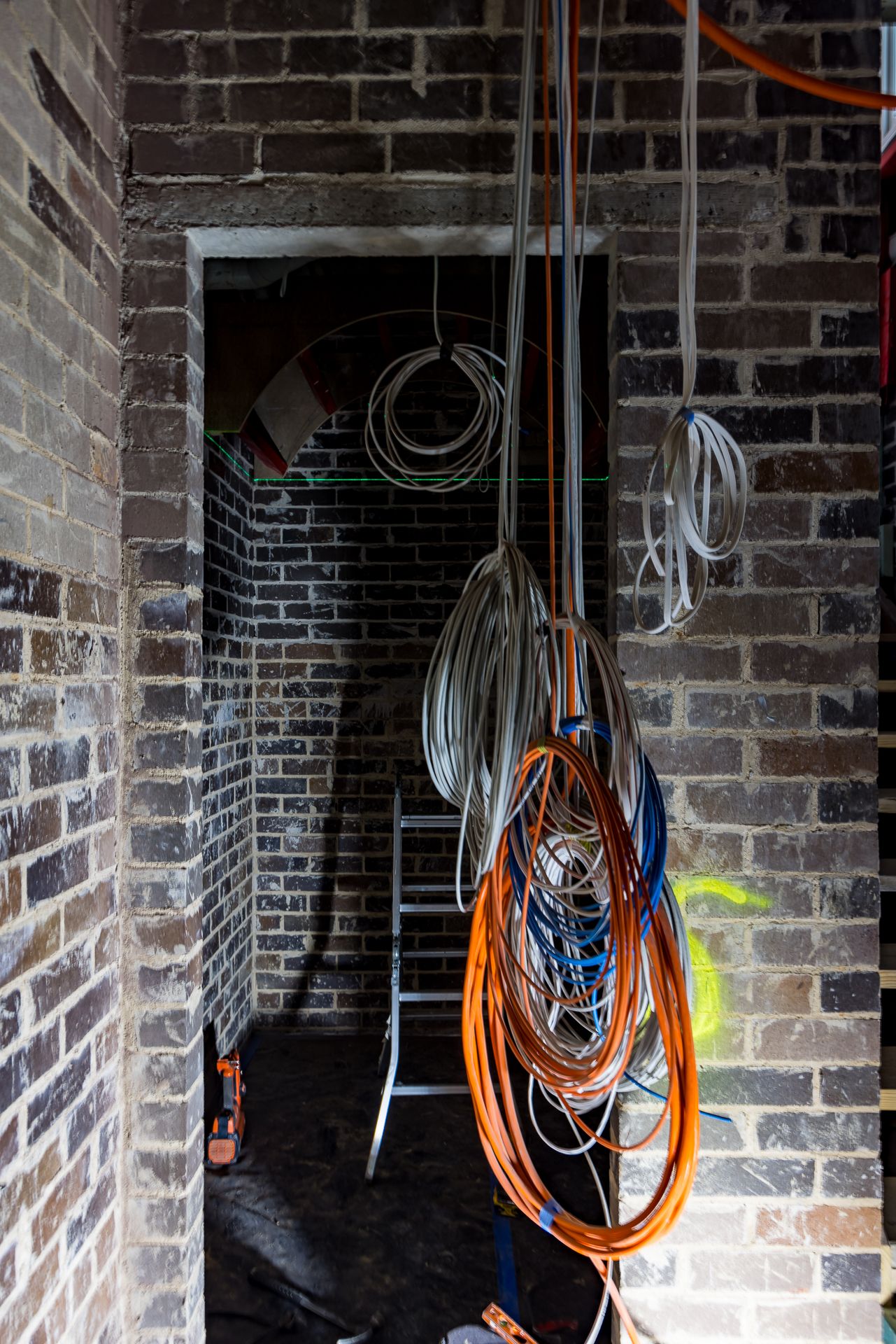 Exposed brick doorway in a renovation site with bundles of orange, blue and white electrical cables hanging from above.