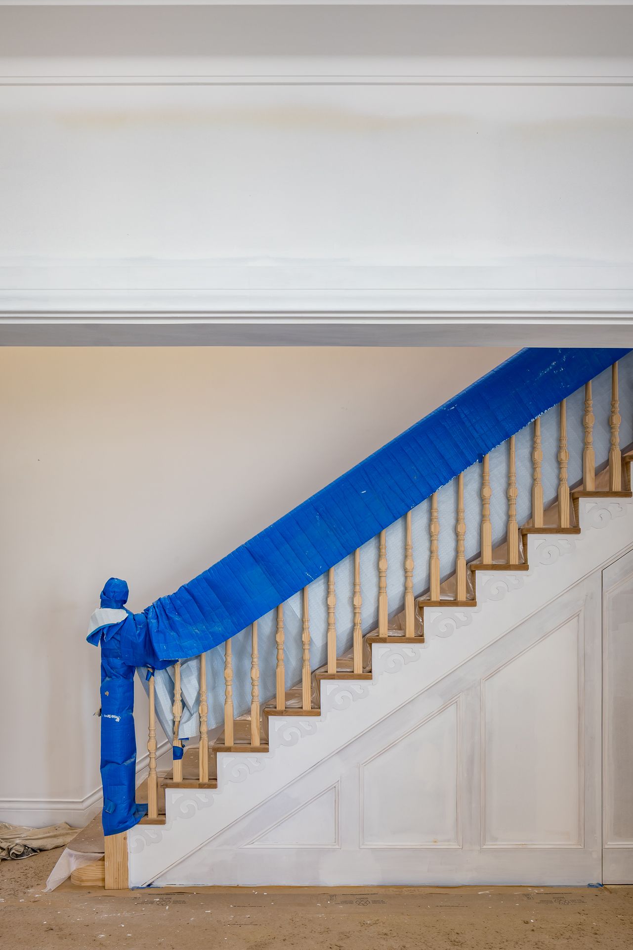 Wooden staircase with turned balusters and handrail wrapped in blue protective covering inside a home under renovation.