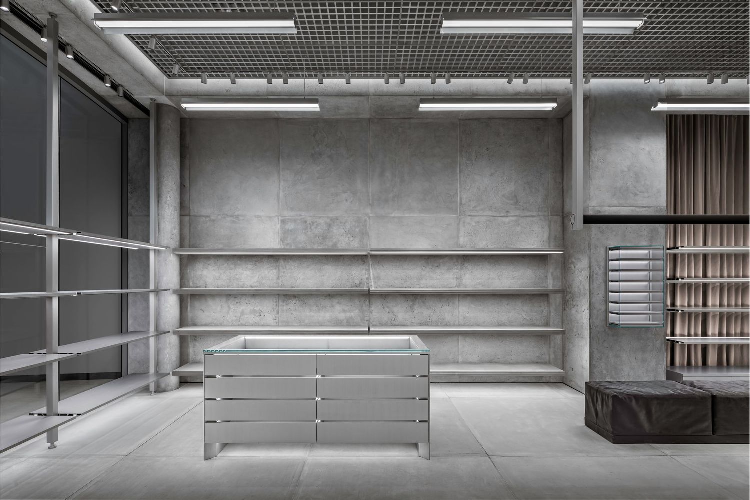 Minimalist concrete retail space with empty metal shelving, a steel display table and industrial ceiling lighting.