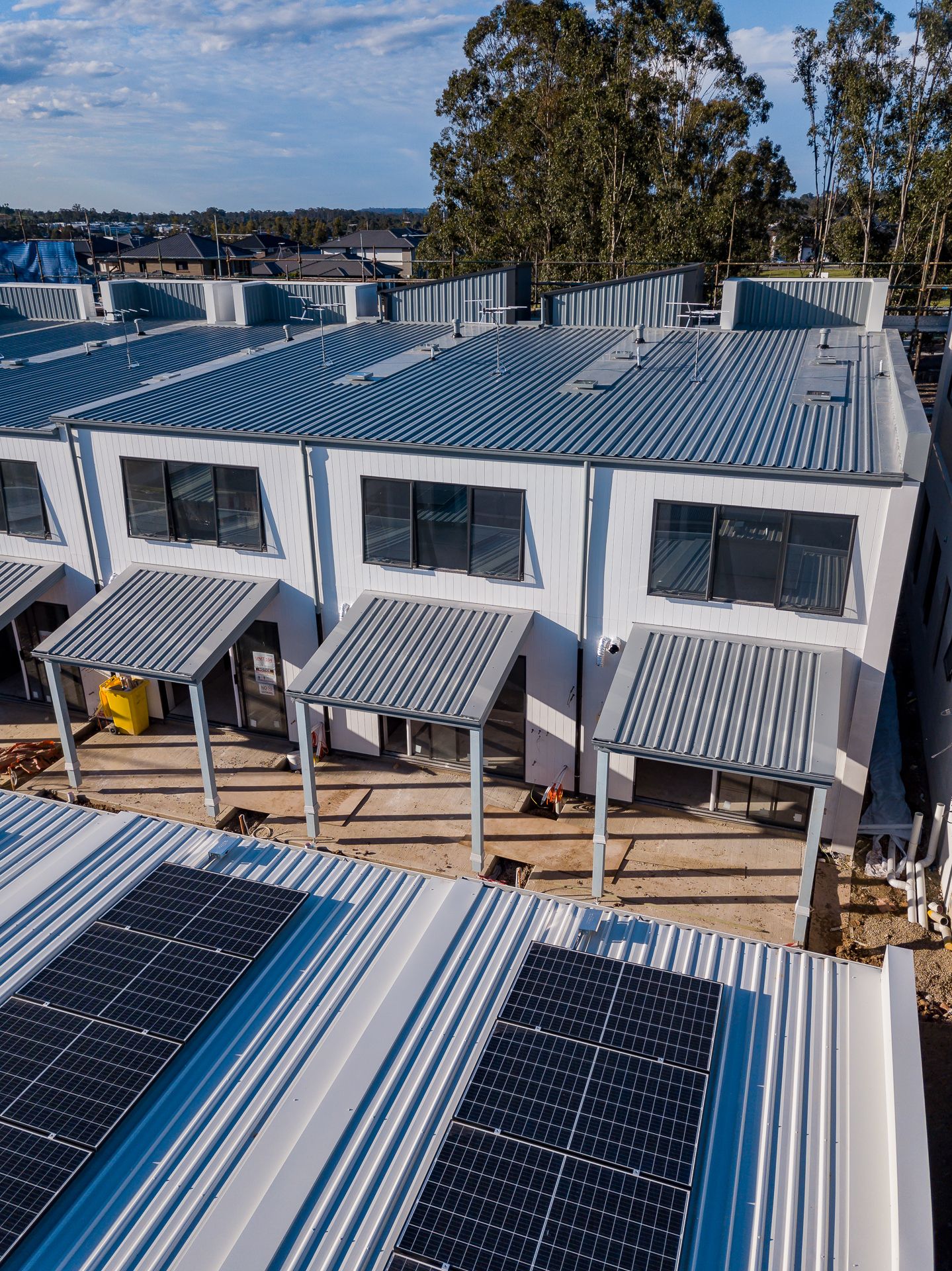 Aerial view of new townhouses with metal roofing, covered patios and solar panels on a residential development site.