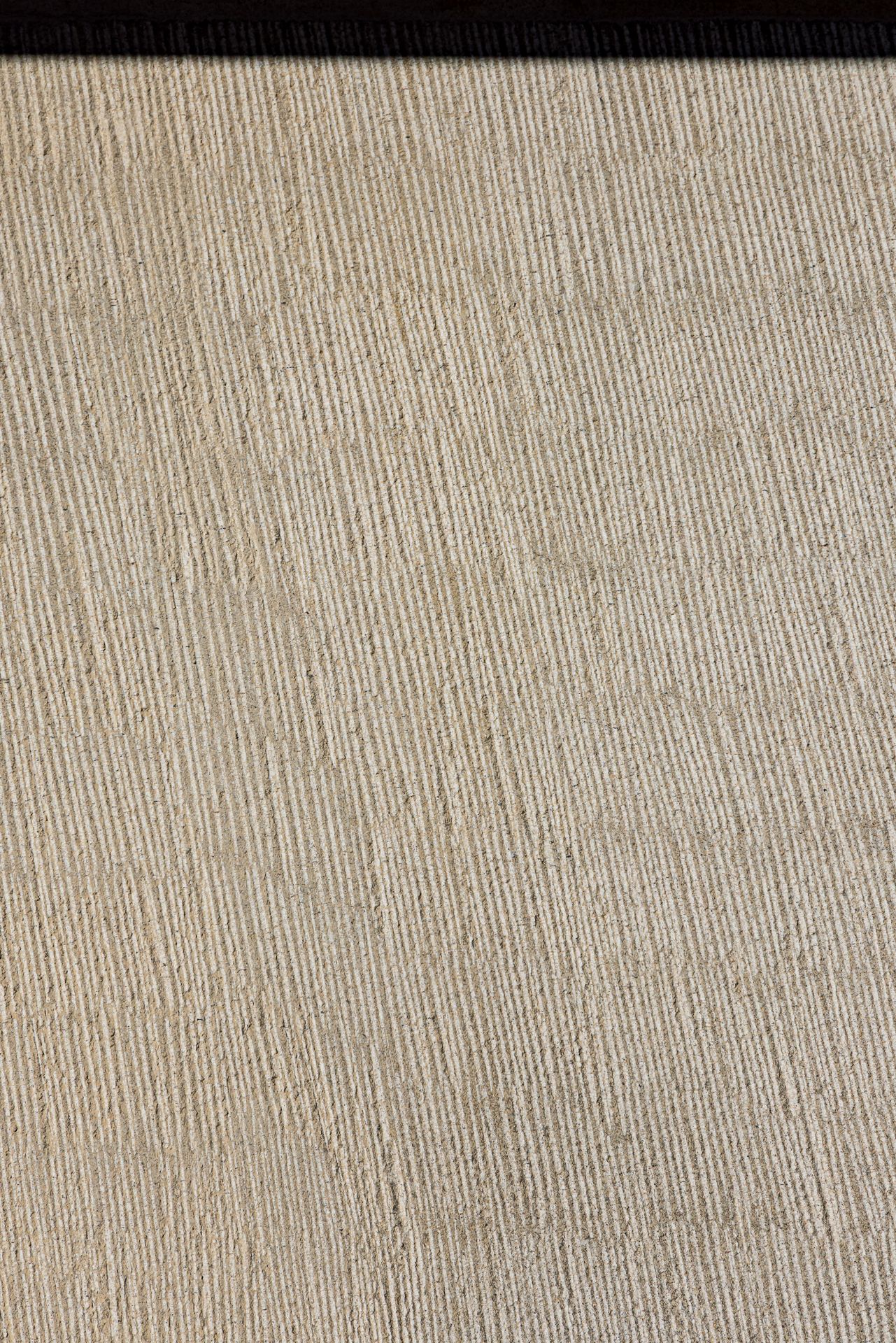 Close-up of pale beige stone surface with fine vertical chiseled grooves creating a ribbed texture.
