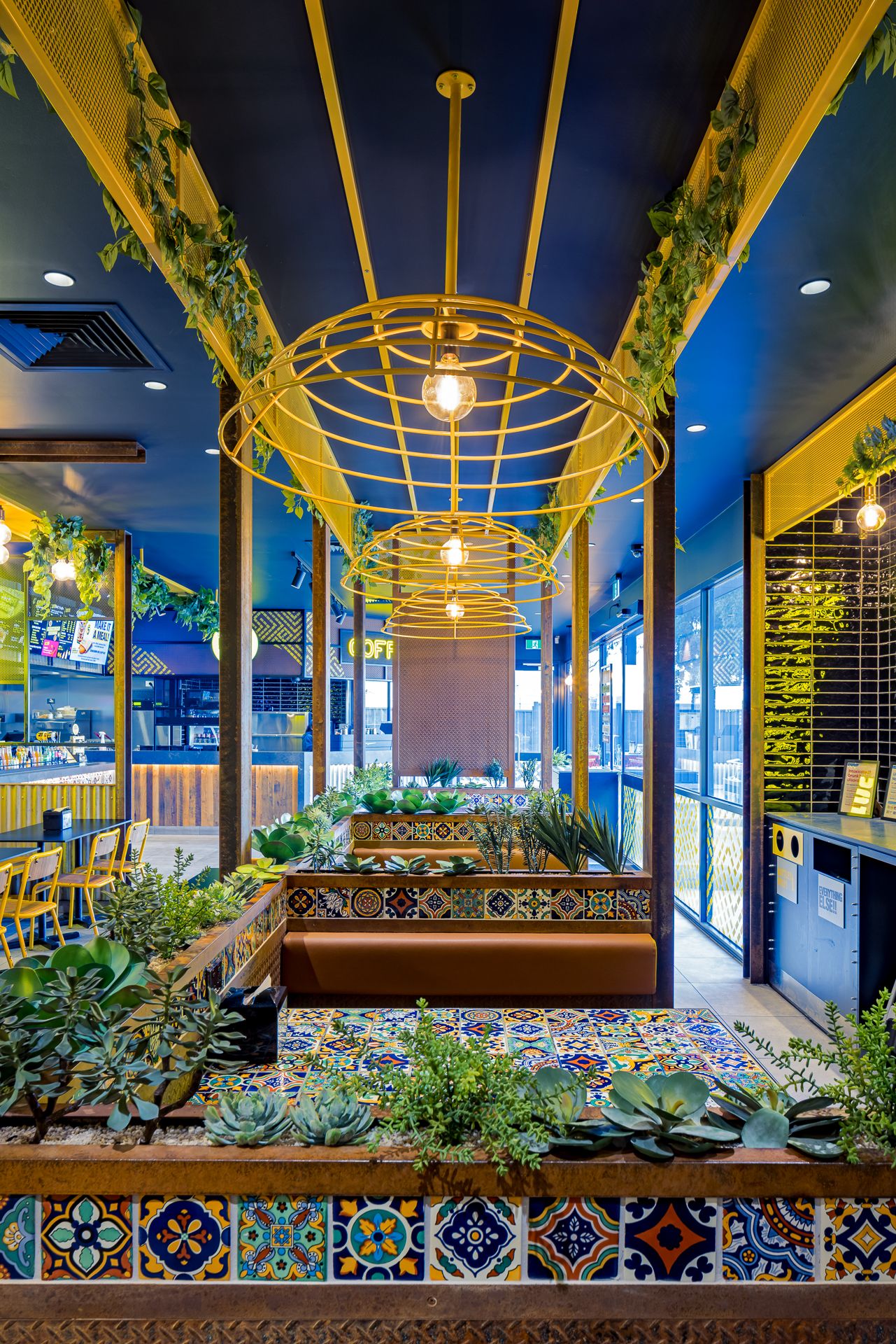 Vibrant Mexican eatery with golden cage pendant lamps, mosaic tiled tables, succulent planters and cozy booth seating.