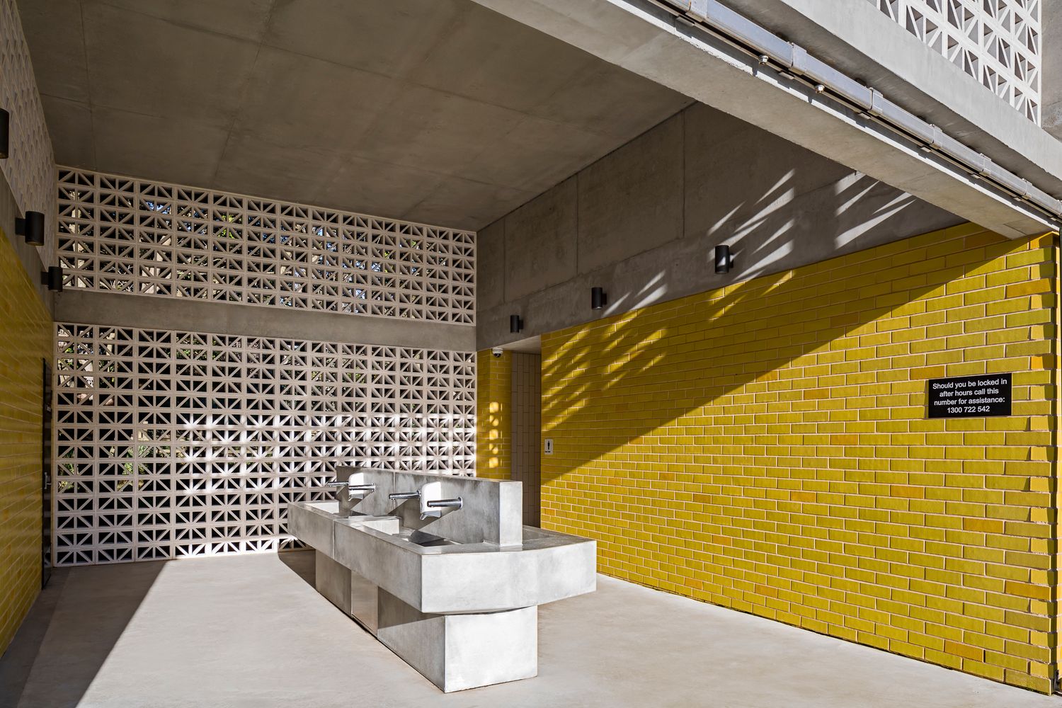 Covered entry of a yellow brick amenities building with breeze block walls, concrete ceiling and a stainless steel washing trough.