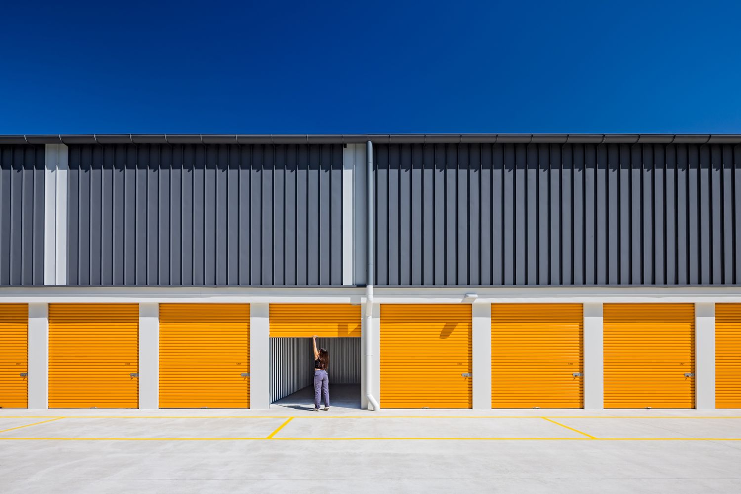 Person standing at an open door among bright orange self storage units under a deep blue sky.