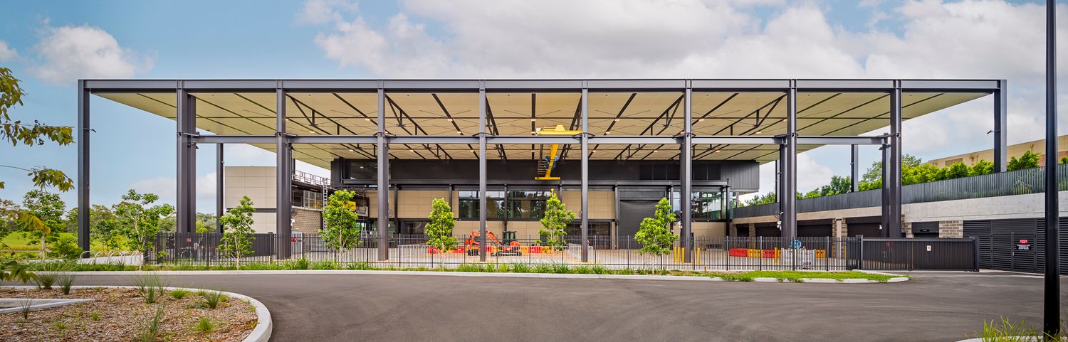 Contemporary single-storey building with a flat steel-framed canopy and landscaped garden beside an empty driveway.