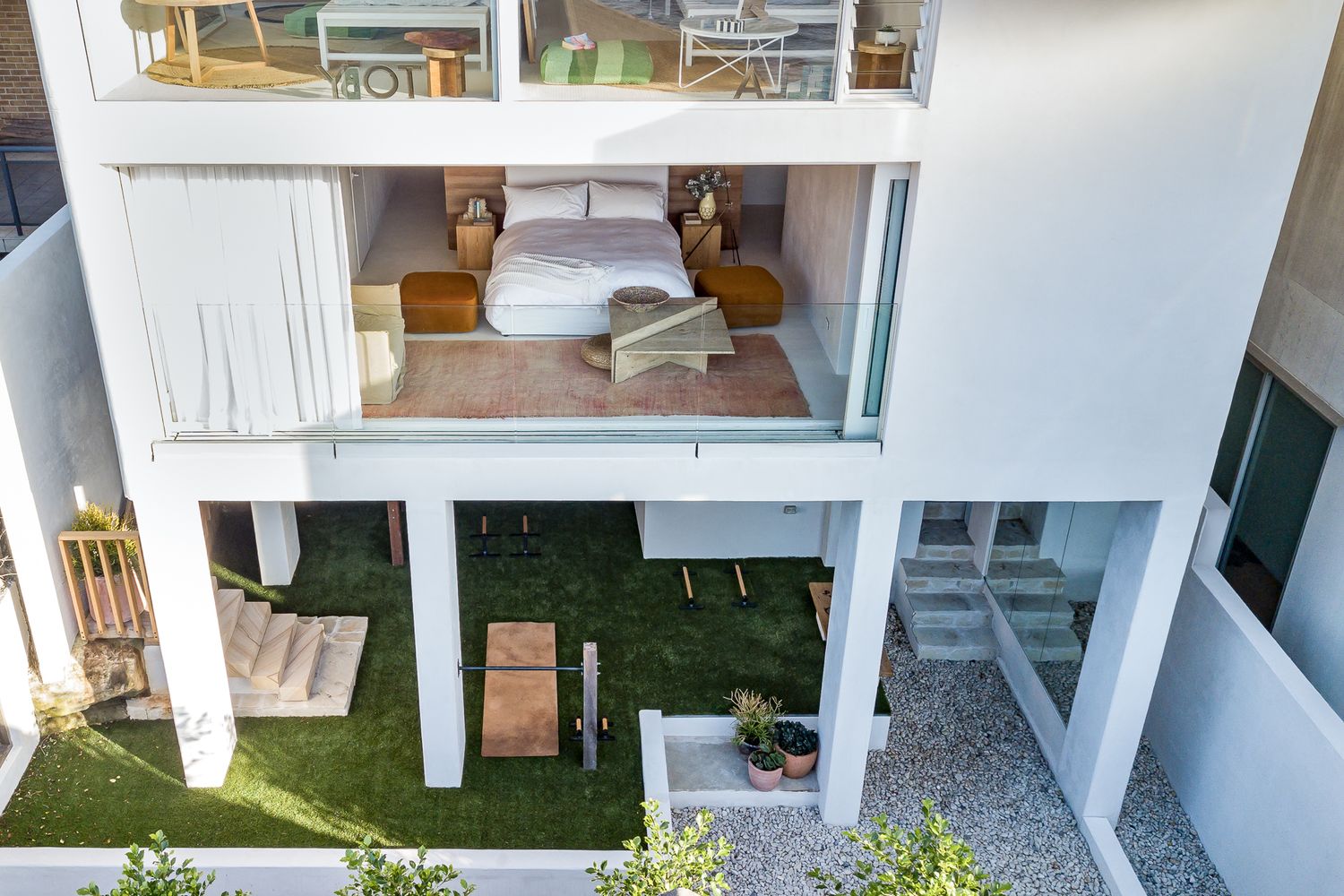 Exterior view of a white modern house showing a bedroom balcony above a lawn and stone patio.