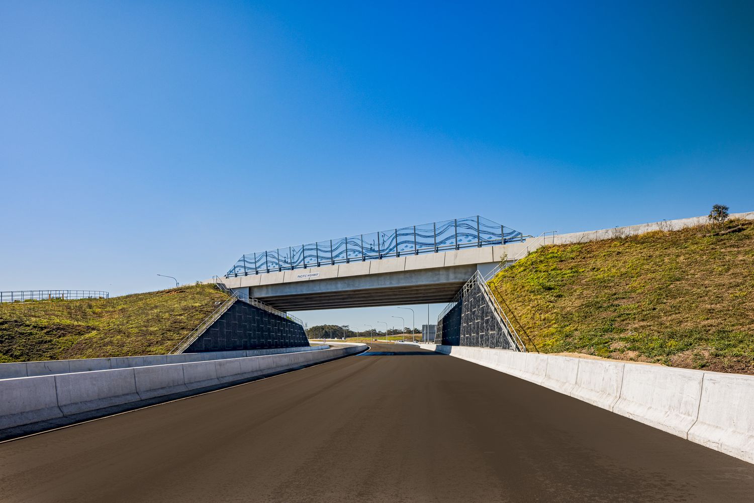 Motorway underpass with stone-faced abutments and a decorative railing on the bridge above, beside grassy embankments.