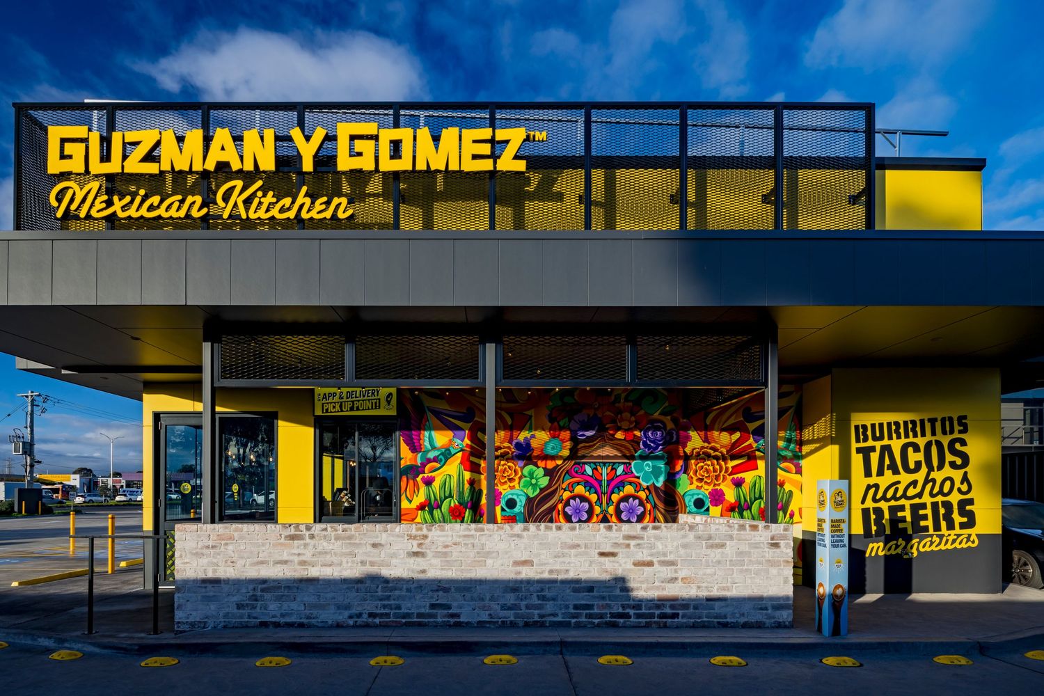 Guzman y Gomez Mexican Kitchen restaurant exterior with bright yellow signage, colorful mural and burritos, tacos and beers sign.