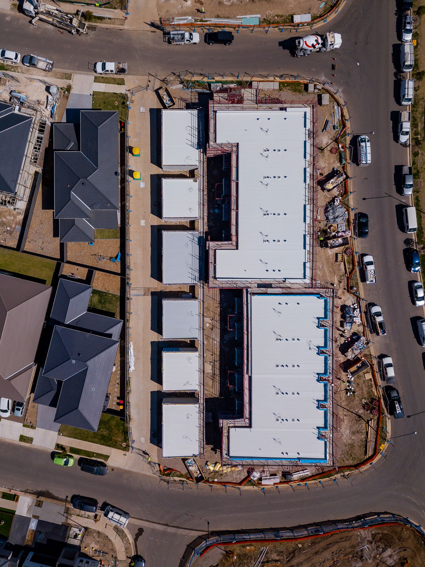 Aerial top-down view of a new townhouse development under construction with flat roofs, surrounding roads and parked vehicles.