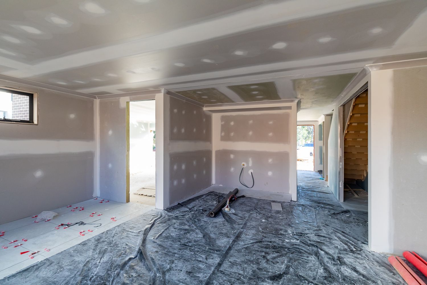 Interior of a new home with plasterboard walls and ceiling, protective plastic sheeting on the floor, and open doorways.