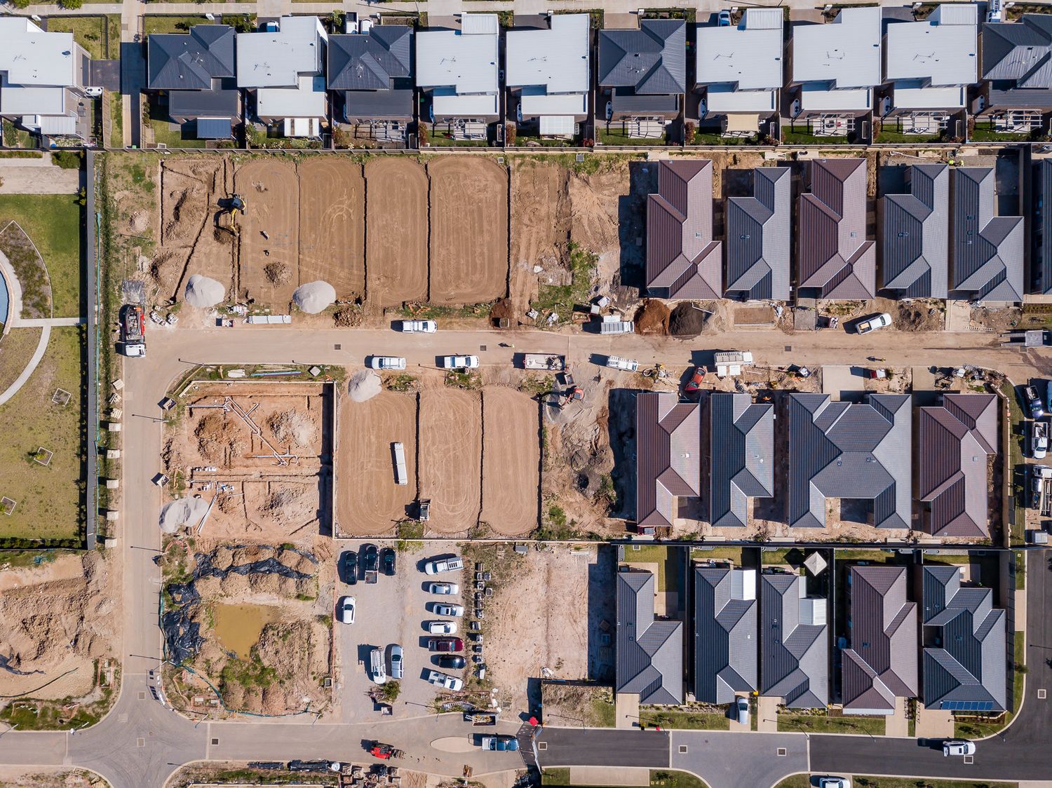 Aerial view of a new residential subdivision with completed townhouses beside vacant dirt lots prepared for further home construction.