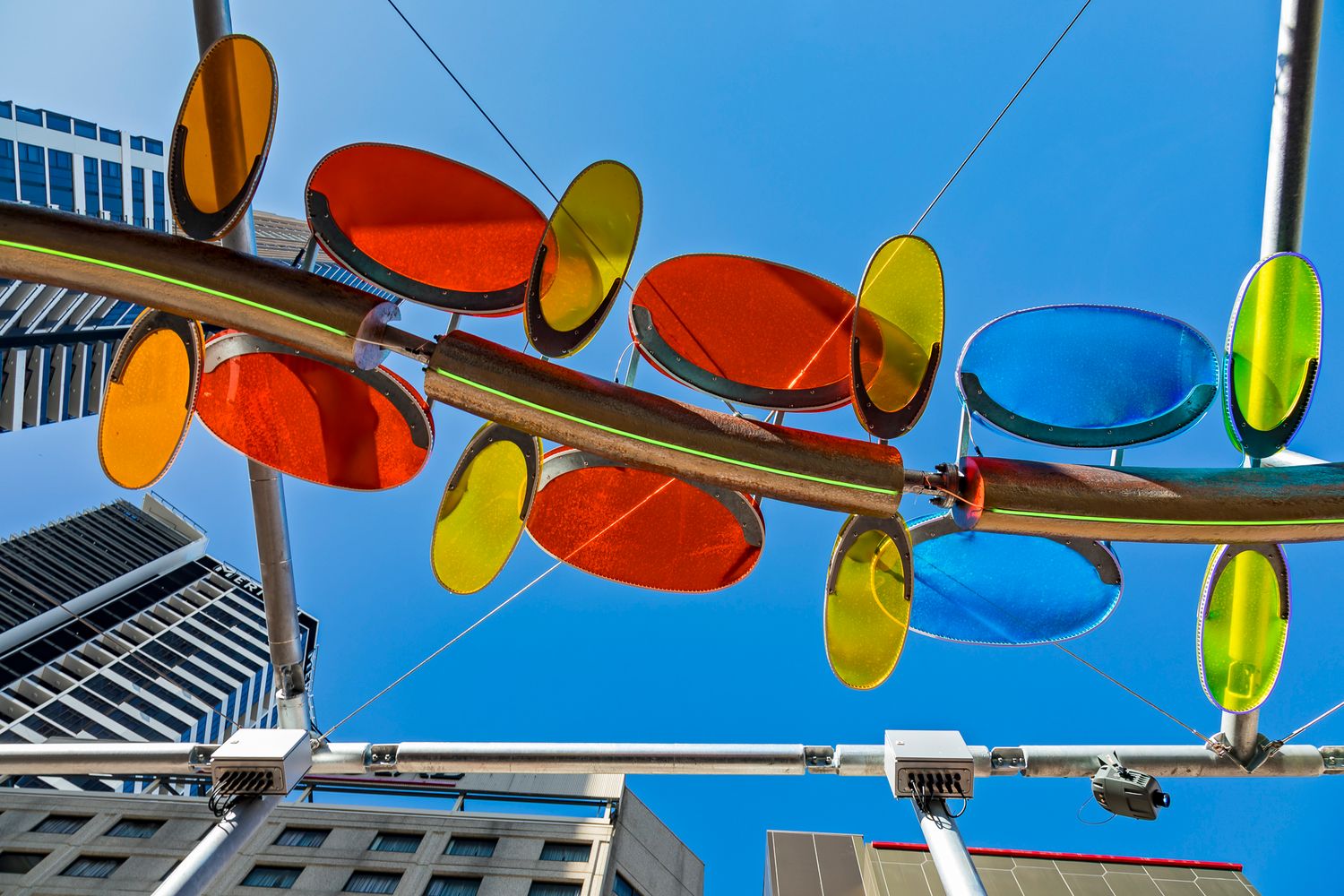Bright yellow, orange, red and blue discs on a long curved metal art installation under a vivid blue sky.
