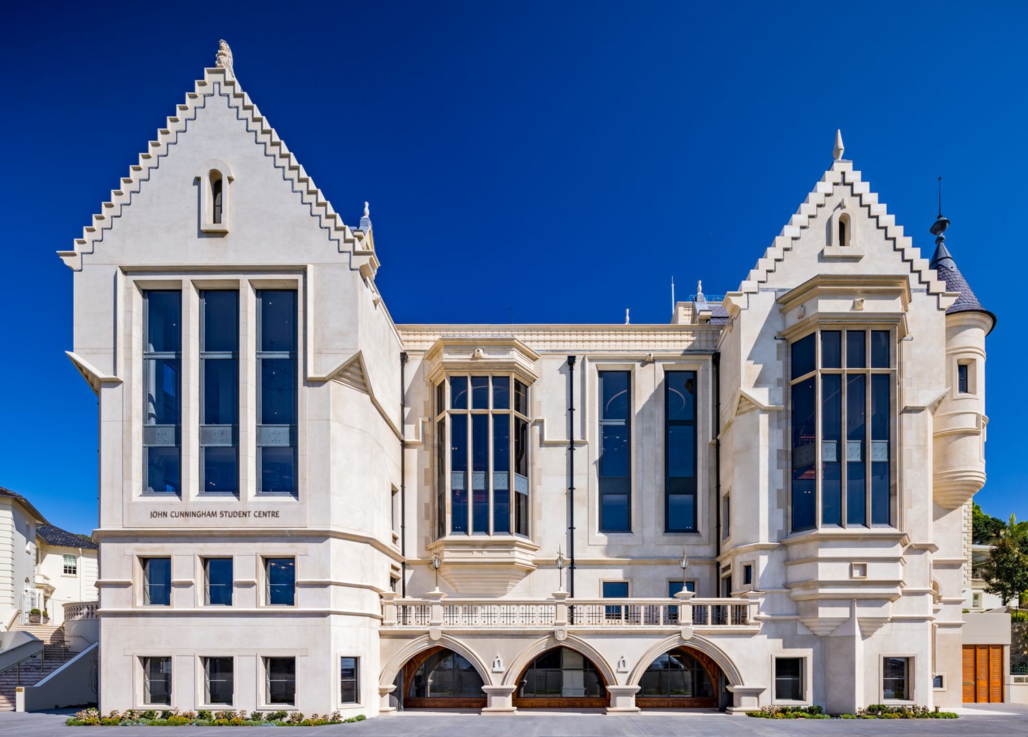 Neo-Gothic stone building with pointed gables, tall arched windows and a balustraded arcade under a bright blue sky.