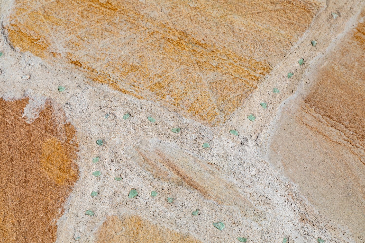 Close-up of textured sandstone paving in warm orange and cream tones with small green flecks embedded in the surface.
