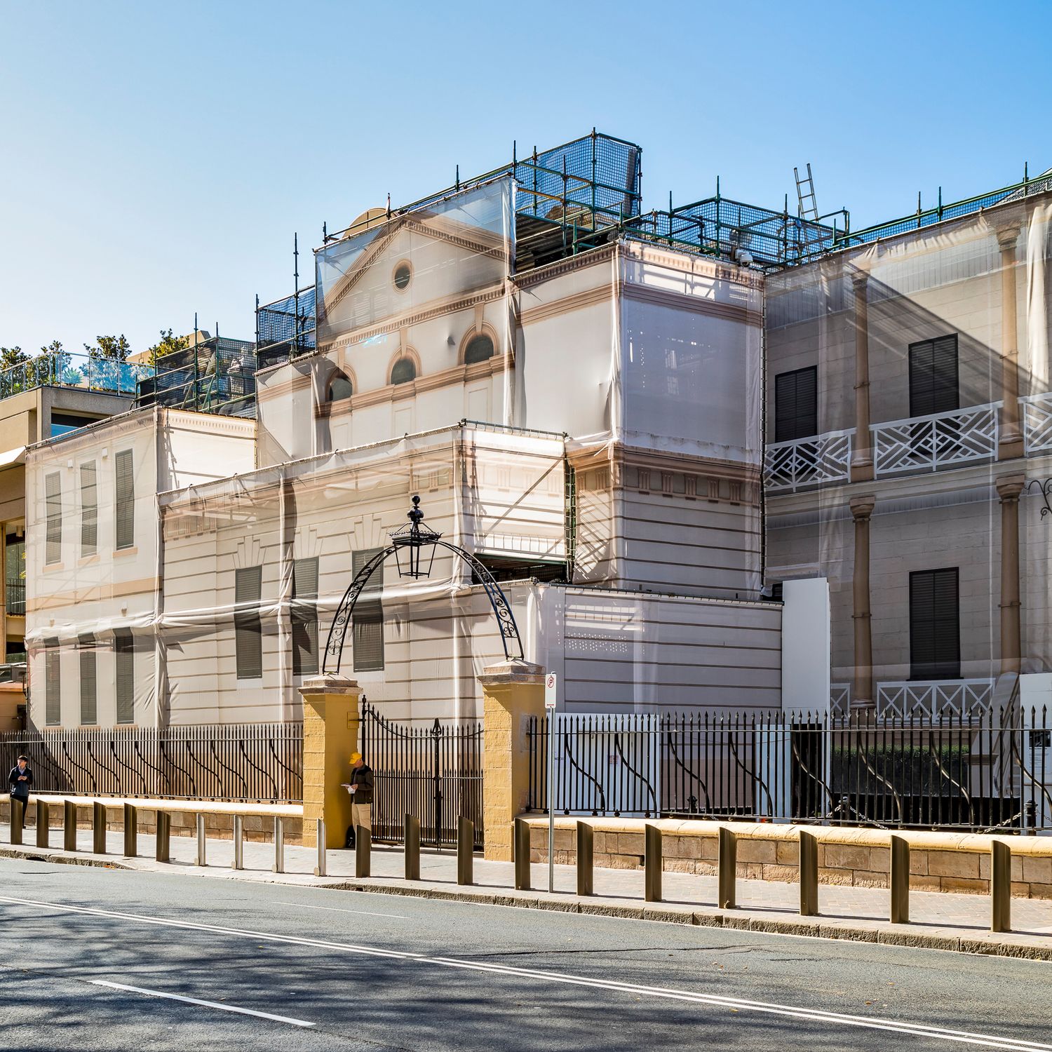 Heritage building wrapped in white protective sheeting and rooftop scaffolding, with a decorative lamp arch over the front gate.