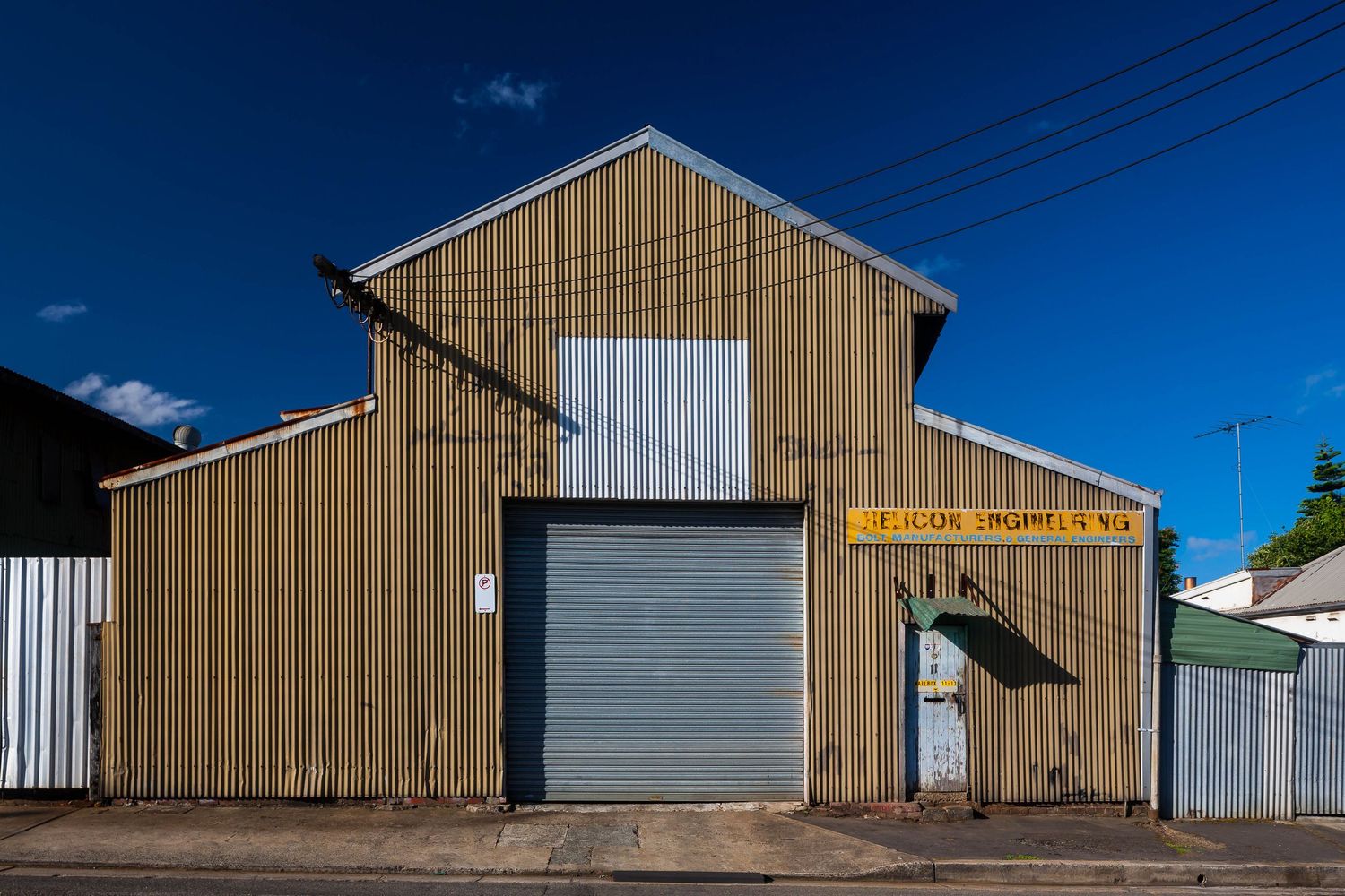 Old rusty corrugated iron workshop with a roller door and a yellow painted sign, set against a deep blue sky.