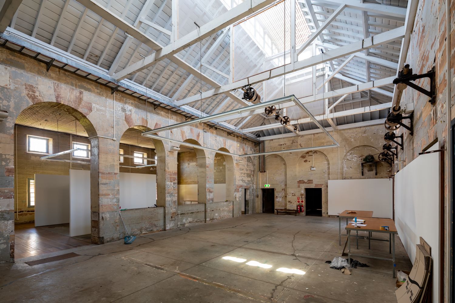 Historic sandstone interior with arched openings and exposed timber roof trusses bathed in natural light from skylights.