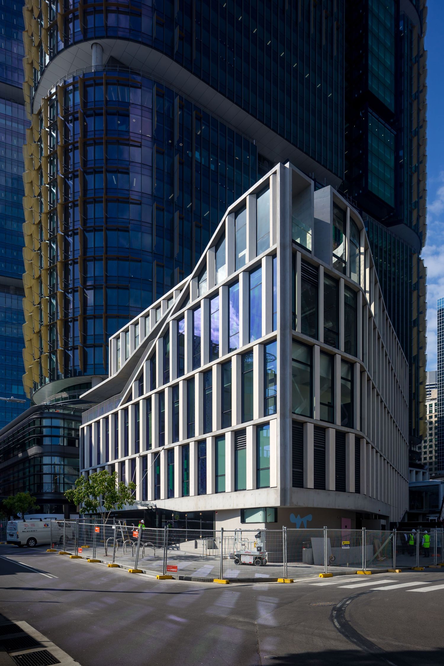 Modern angular glass and white-framed building with a sculptural roofline beside a dark glass skyscraper on a city street.
