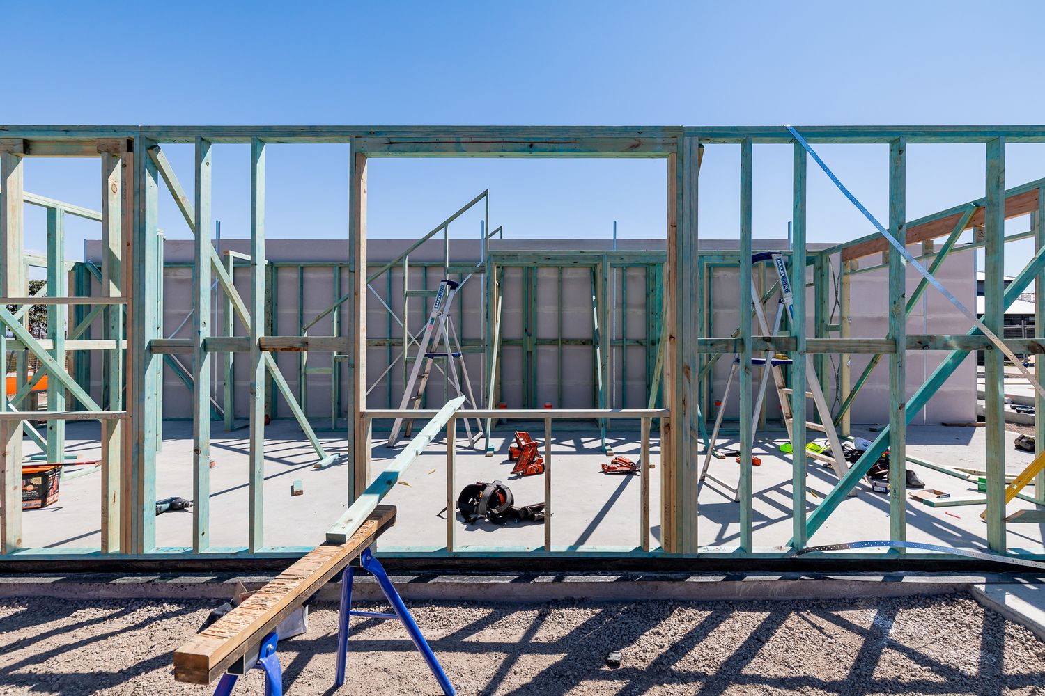 Timber and steel wall framing of a townhouse under construction with scaffolding and building materials visible against a blue sky.