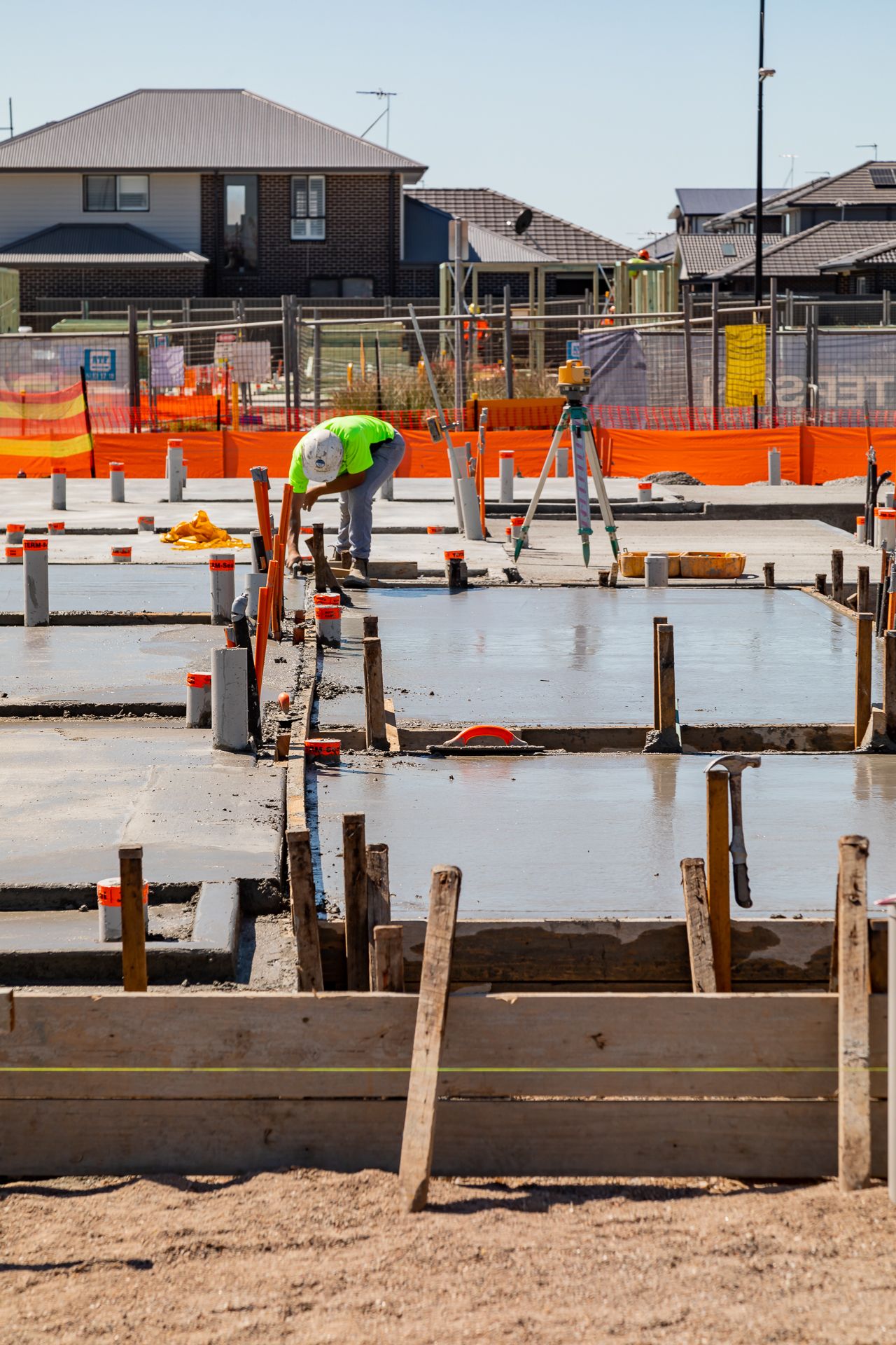 A worker in a hi-vis vest inspects freshly poured concrete slabs with timber formwork at a housing development site.