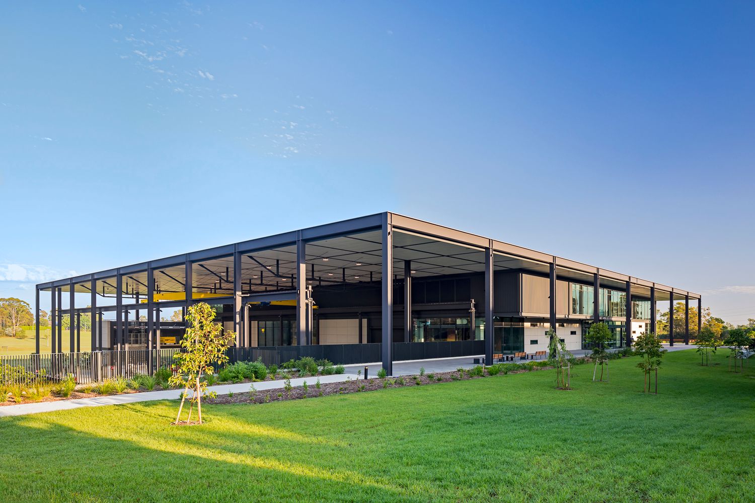 Contemporary TAFE workshop building with an open steel structure and large glass facade overlooking a green lawn at sunset.