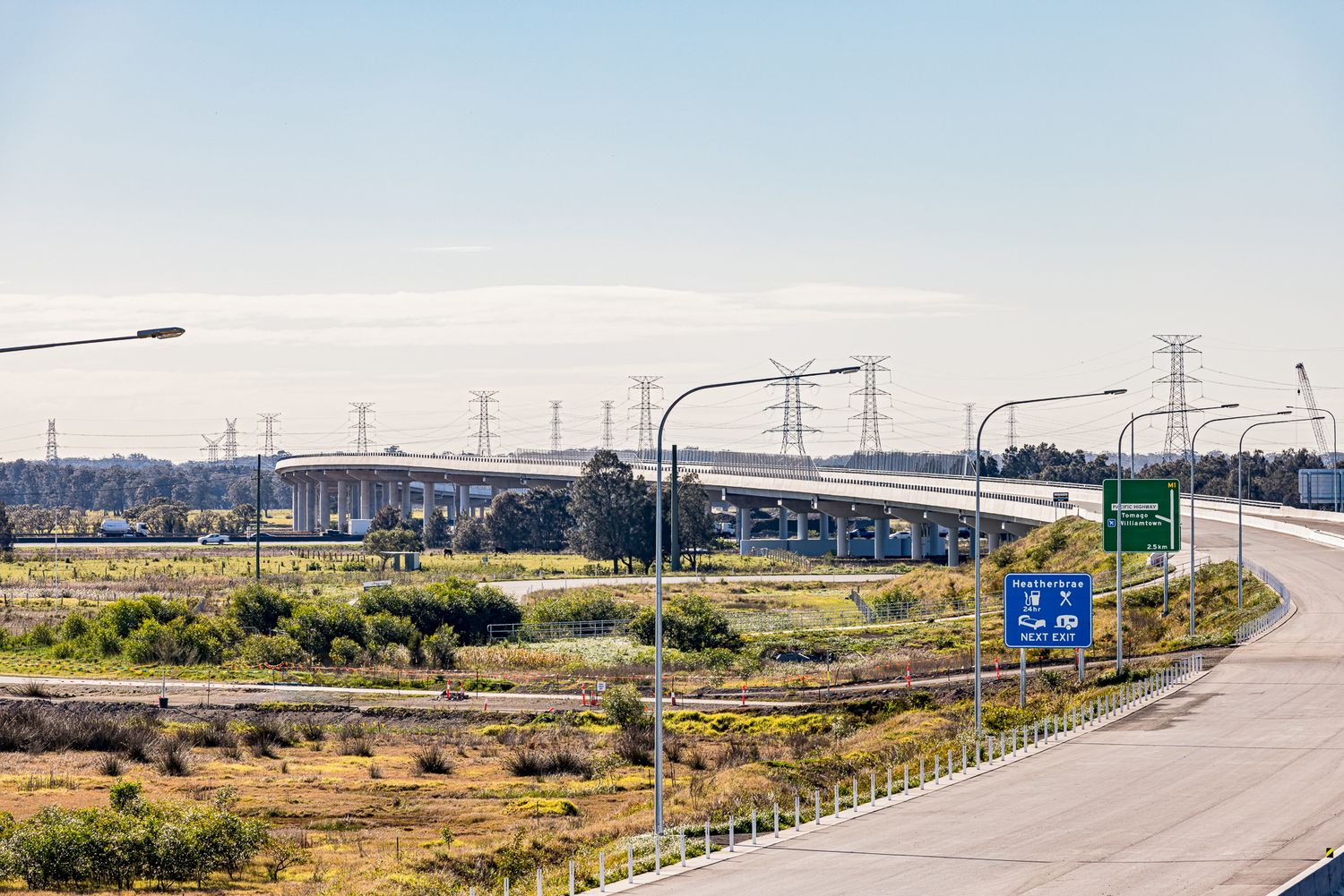 Elevated highway interchange with street lights, green and blue road signs, and power pylons stretching across the distant landscape.