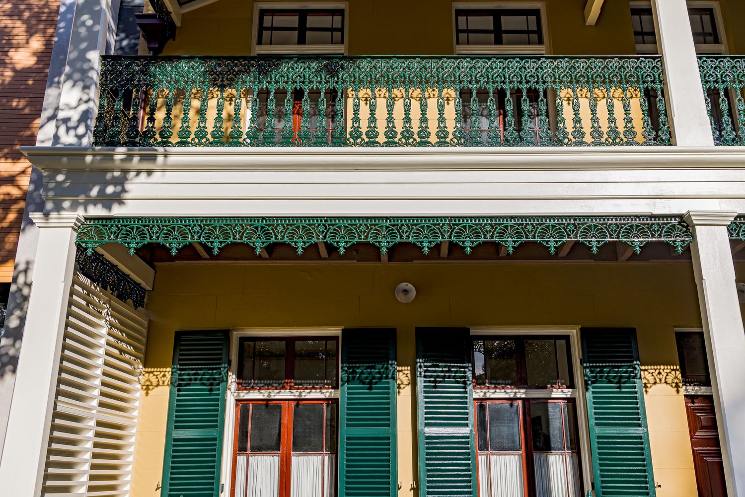 Heritage terrace facade with green cast-iron lace balcony, white columns, green timber shutters and yellow walls.