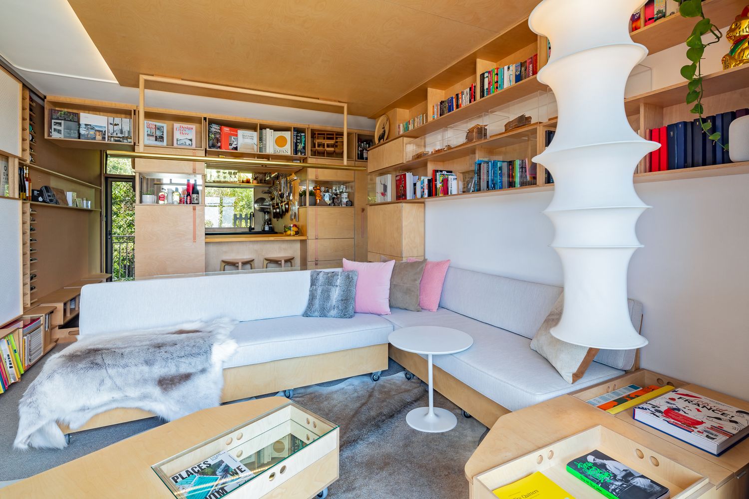 Small living space with custom timber shelving, a pendant paper lamp, a cushioned built-in sofa, and a storage coffee table.