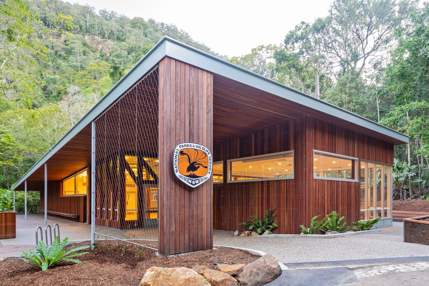 Contemporary timber-clad building with a wide sloping roof and circular bird emblem, nestled among bushland and native plants.