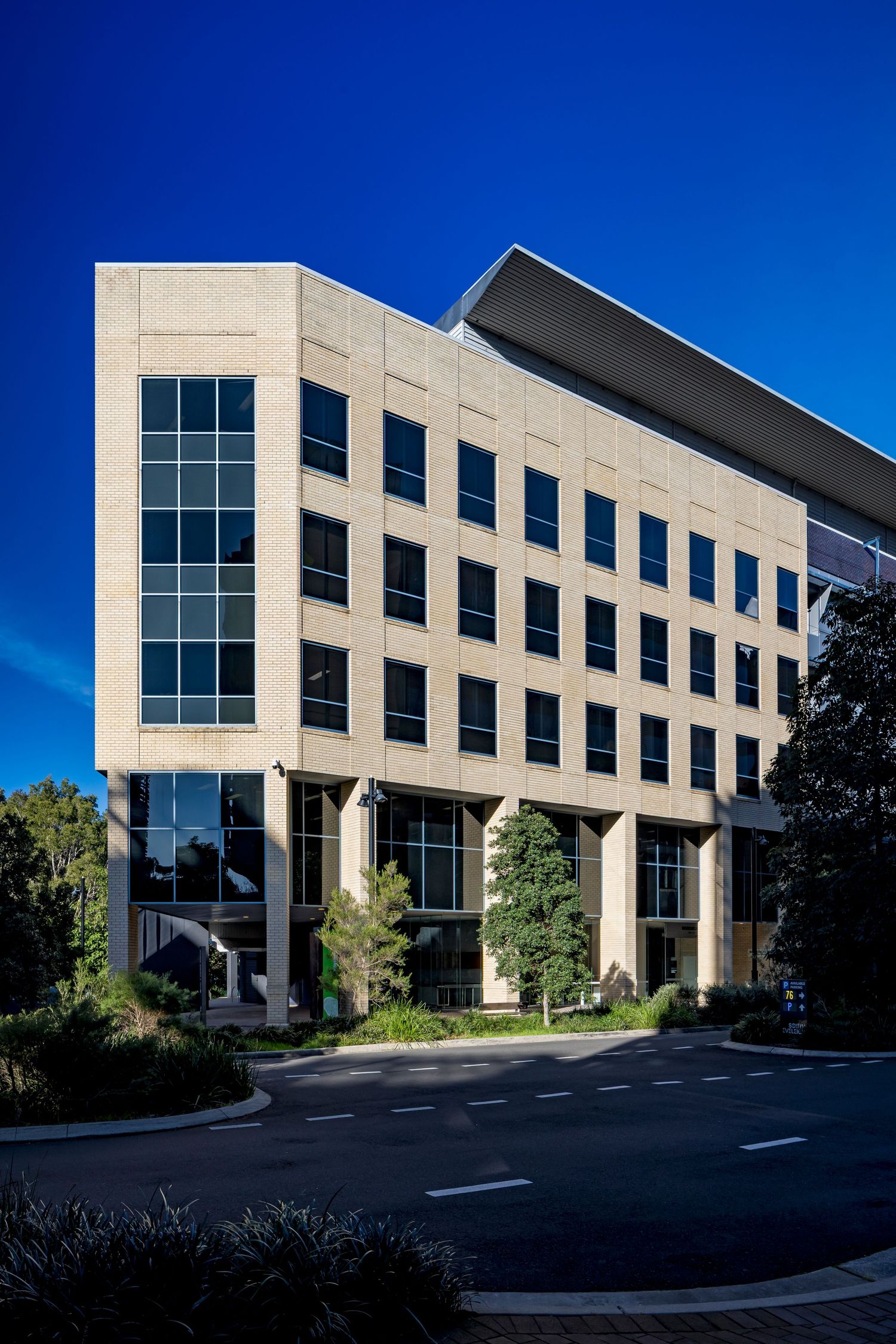 Multi-storey stone-clad office building with large windows and a sloping roof, set against a vivid blue sky.