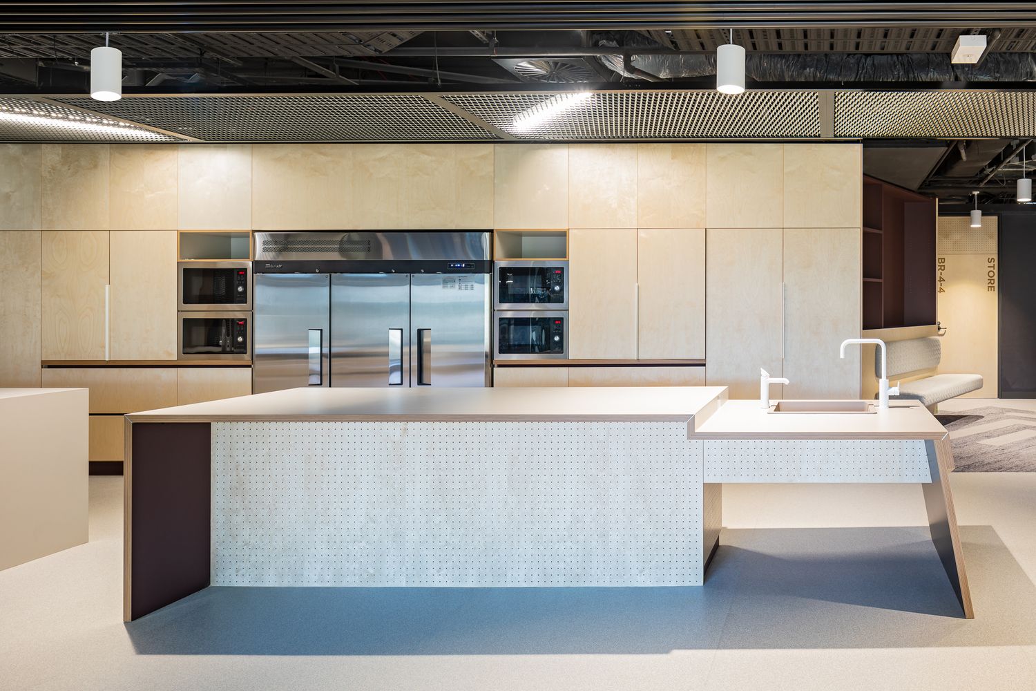 Contemporary office kitchen with large stone-textured island, stainless steel double-door fridge, built-in ovens and beige cabinetry.