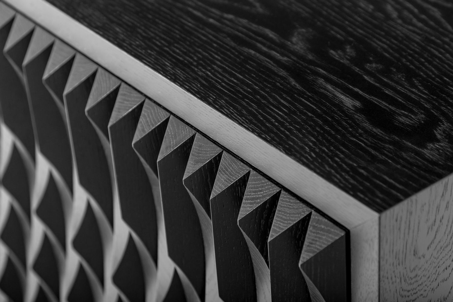 Close-up of a black wooden cabinet with a textured, three-dimensional sawtooth pattern and visible wood grain.