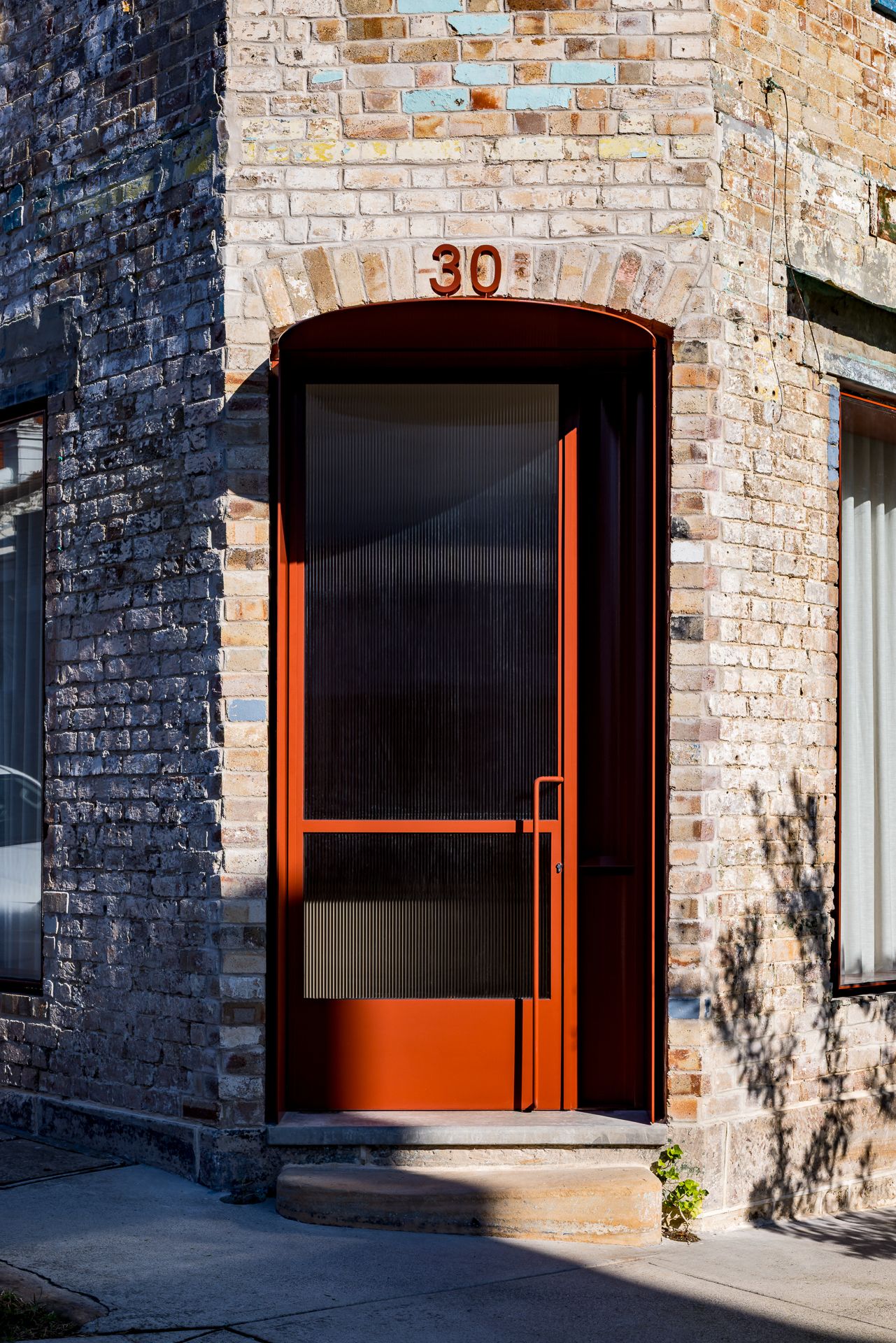 Arched red entry door with reeded glass and number 30 set into a weathered brick facade with painted accents.