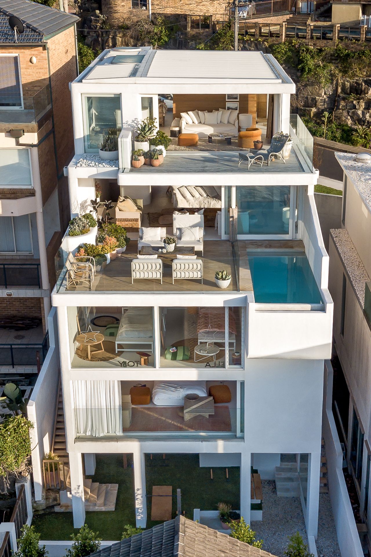 Multi-level white modern home with terraces, plants, and a rooftop pool, viewed from above.