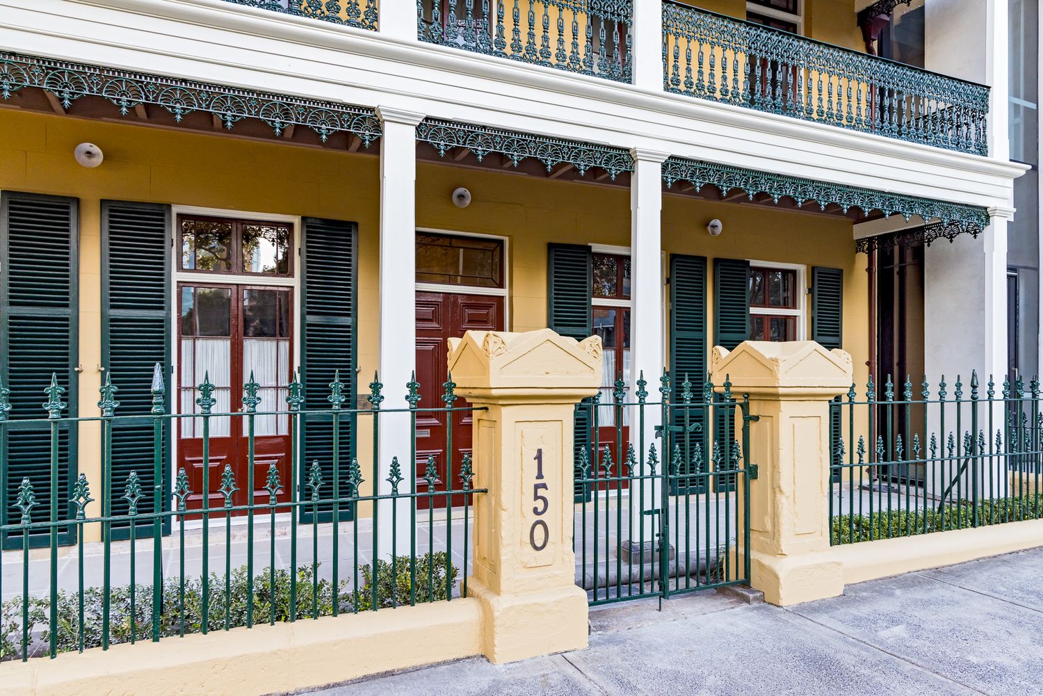 Heritage terrace entrance with green iron fence, stone gate pillars marked number 150, and lace-trimmed verandah.