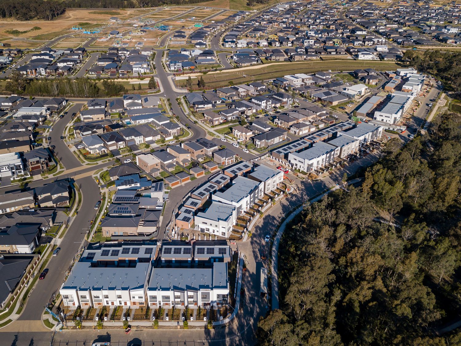 Aerial view of a new suburban housing development with townhouses, winding streets, and bushland on the edge of the estate.