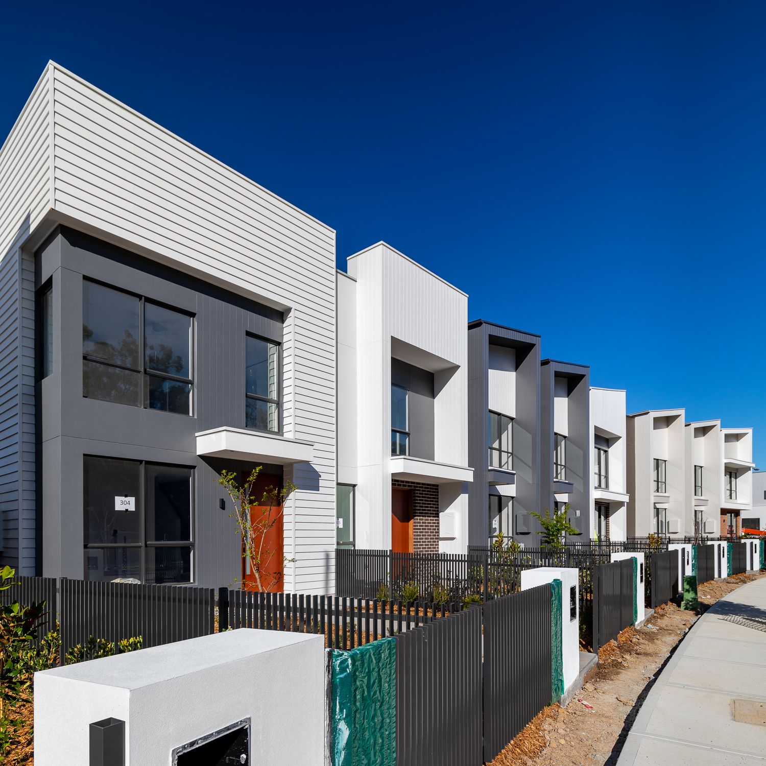 Contemporary terrace townhouses with grey and white facades, orange doors and black fencing along a new residential street.