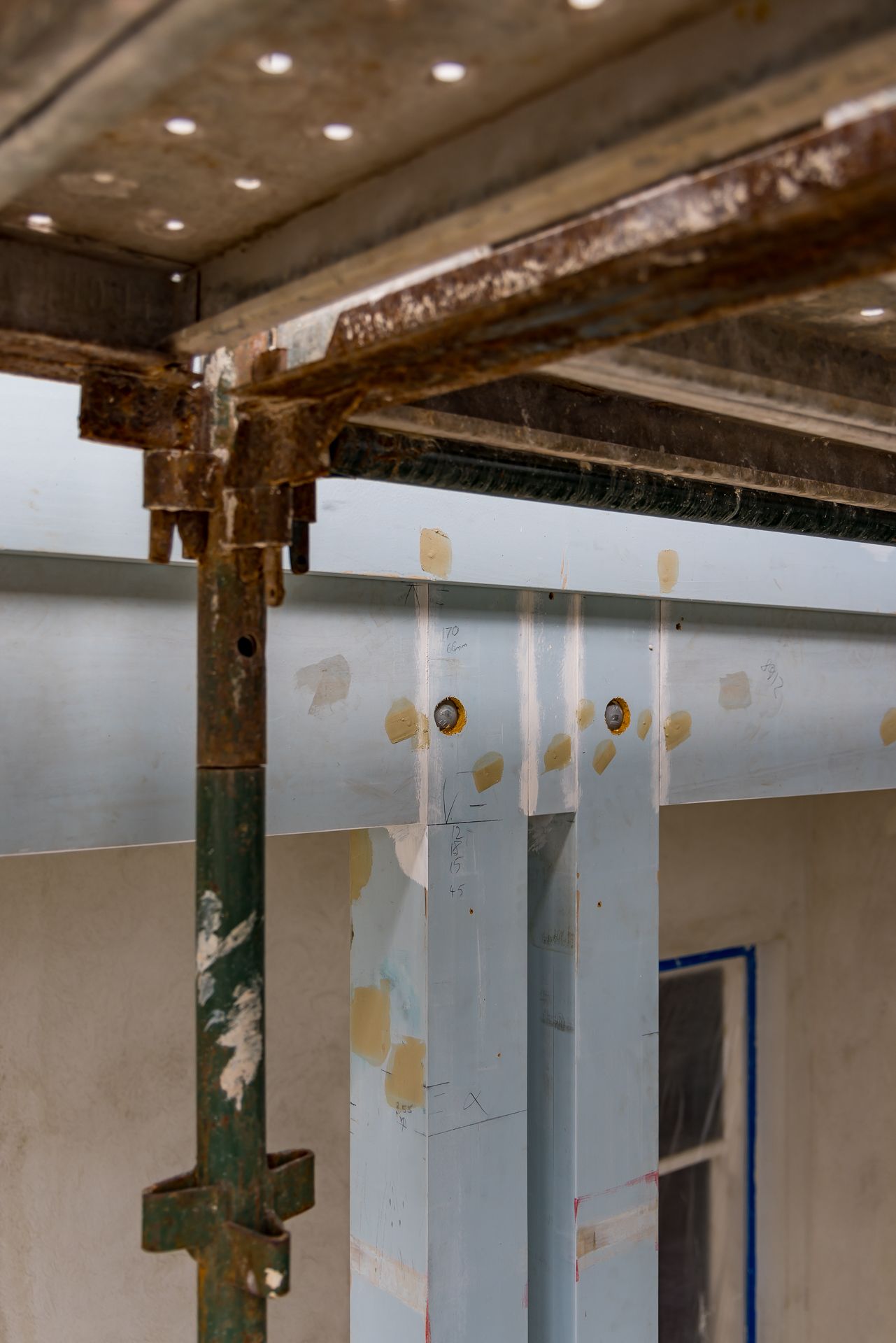 Close-up of scaffolding and steel support beams with painted blue panels at a building renovation site.