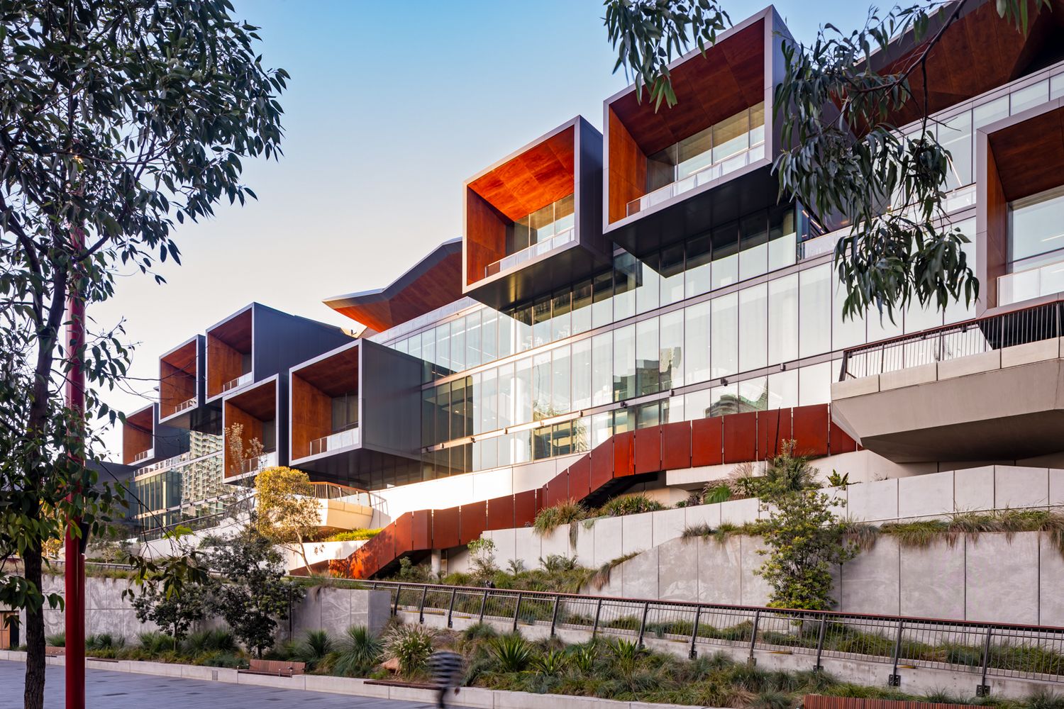 Contemporary terraced building with warm timber-clad balconies and glass facades stepping down a landscaped hillside.