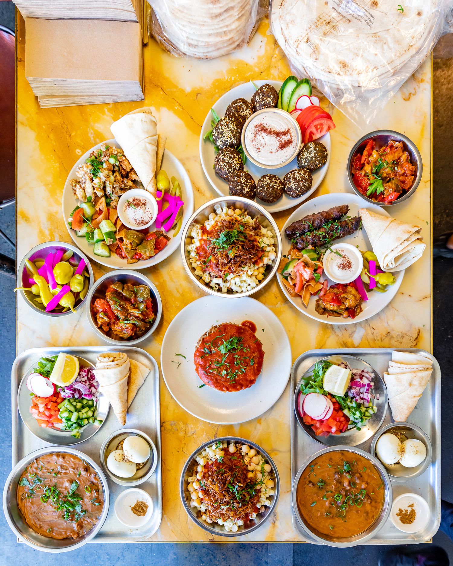 Overhead view of a Middle Eastern mezze spread with falafel, hummus, salads, flatbread, and dips on a yellow marble table.