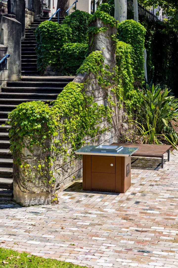 Ivy-covered stone wall beside stone steps and a brick paved courtyard with a brown cabinet and wooden bench.