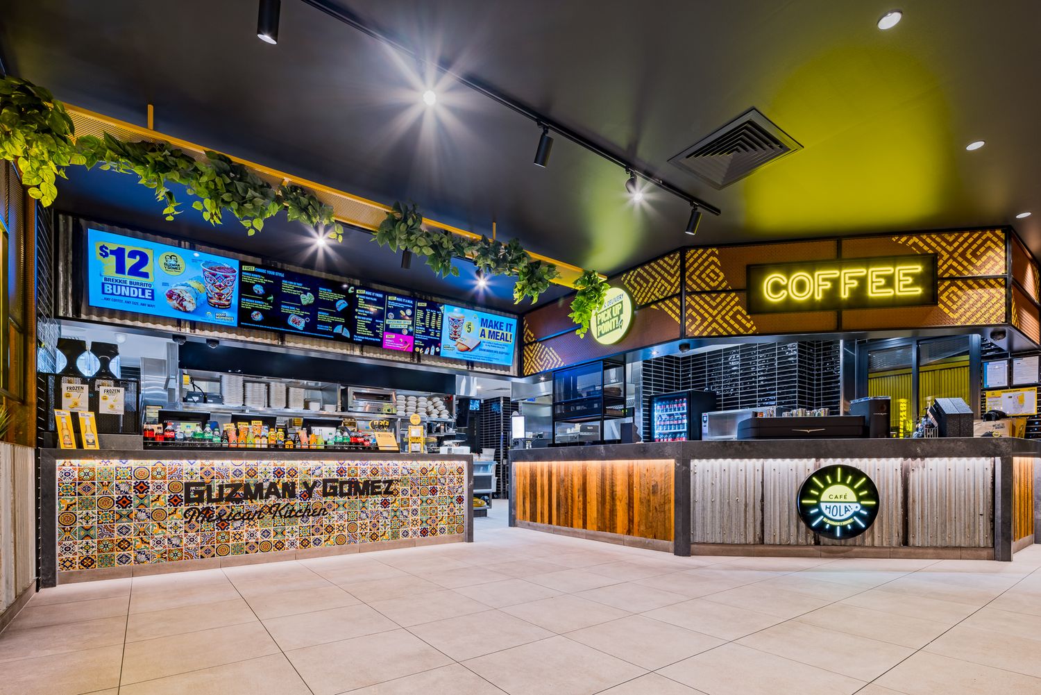 Modern Guzman y Gomez restaurant interior with tiled counter, digital menu boards, hanging plants and a coffee bar.